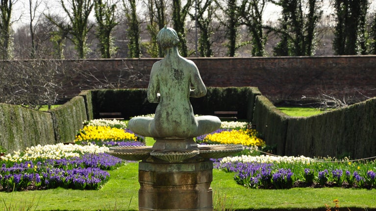 Looking down the long spring flower borders with the back of the fountain statue in the foreground
